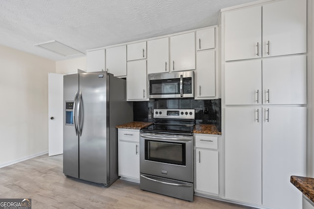 kitchen featuring appliances with stainless steel finishes, dark stone countertops, white cabinetry, decorative backsplash, and light wood-type flooring