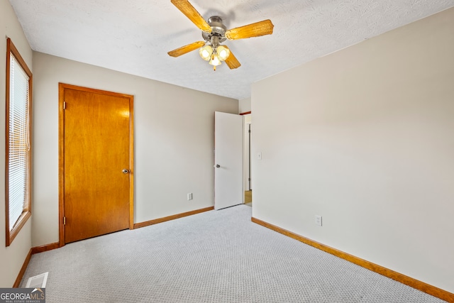 unfurnished bedroom featuring ceiling fan, light colored carpet, and a textured ceiling