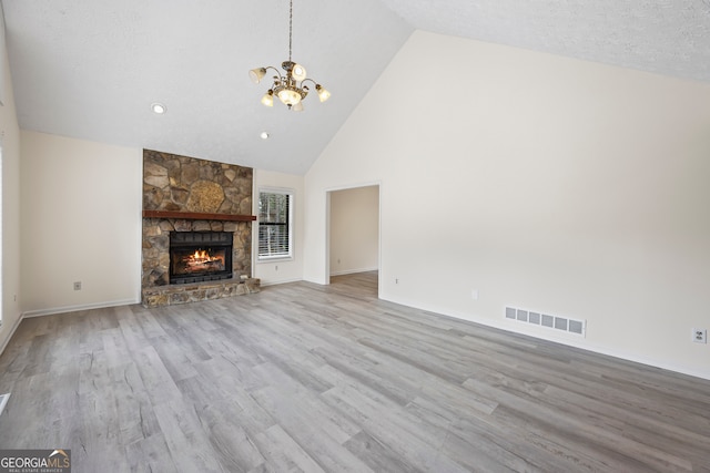 unfurnished living room with a notable chandelier, a stone fireplace, light hardwood / wood-style floors, and high vaulted ceiling