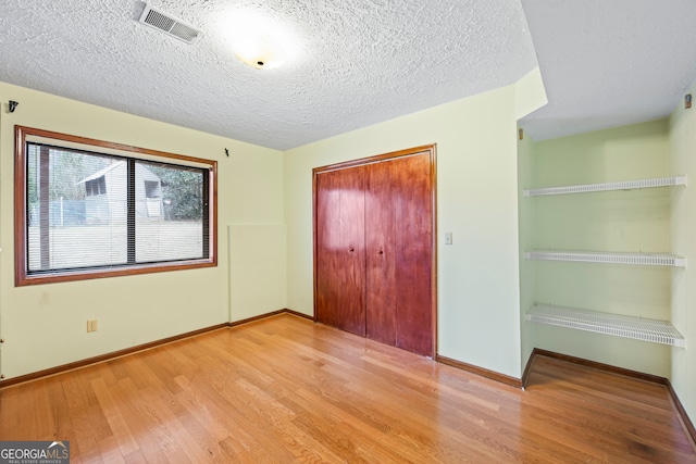 unfurnished bedroom featuring a textured ceiling, a closet, and light wood-type flooring