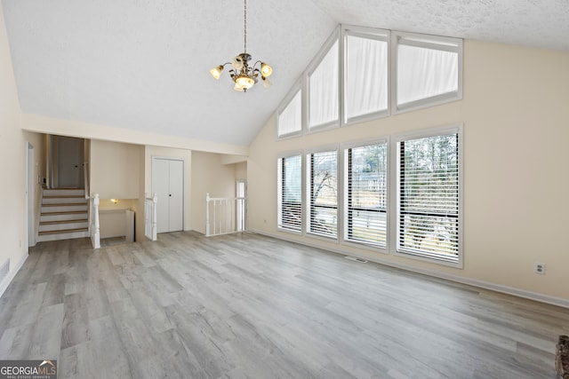 unfurnished living room featuring high vaulted ceiling, a textured ceiling, a chandelier, and light hardwood / wood-style floors