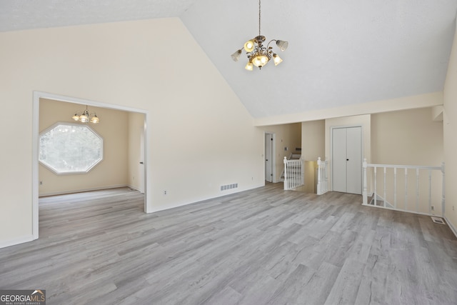 unfurnished living room with high vaulted ceiling, an inviting chandelier, and light hardwood / wood-style flooring