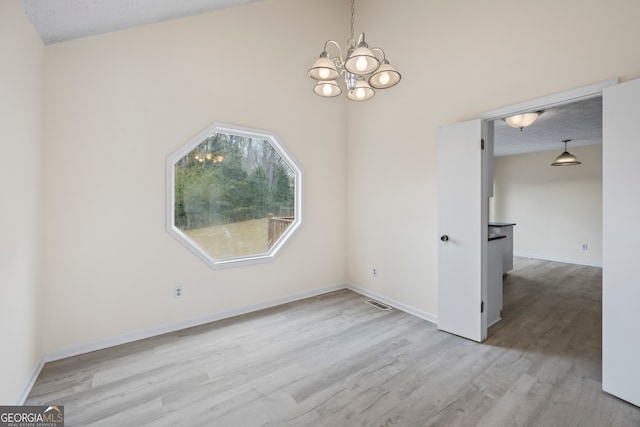 unfurnished dining area with an inviting chandelier, a textured ceiling, and light wood-type flooring