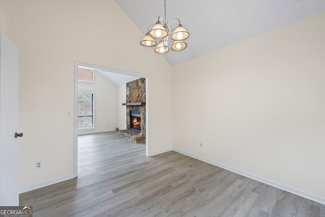 unfurnished dining area featuring an inviting chandelier, a stone fireplace, light hardwood / wood-style floors, and vaulted ceiling