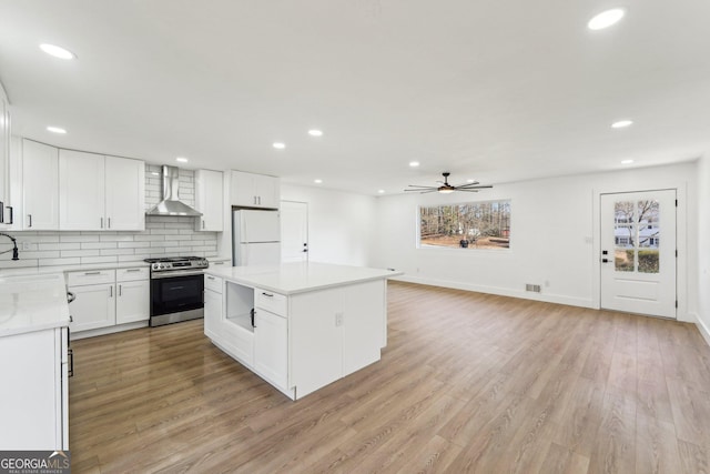 kitchen with wall chimney exhaust hood, white cabinetry, stainless steel range with gas cooktop, a kitchen island, and white fridge