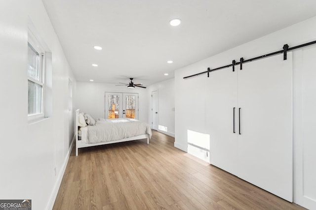 unfurnished bedroom featuring a barn door, ceiling fan, and light wood-type flooring