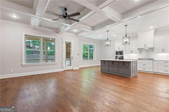 kitchen featuring pendant lighting, a kitchen island with sink, white cabinetry, coffered ceiling, and ceiling fan with notable chandelier