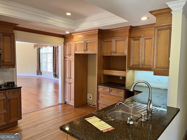 kitchen with ornate columns, a tray ceiling, light wood-type flooring, and dark stone counters