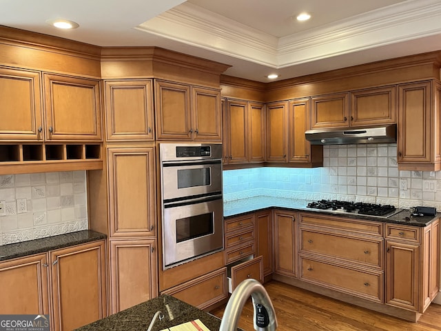 kitchen with gas stovetop, light wood-type flooring, a tray ceiling, double oven, and dark stone counters