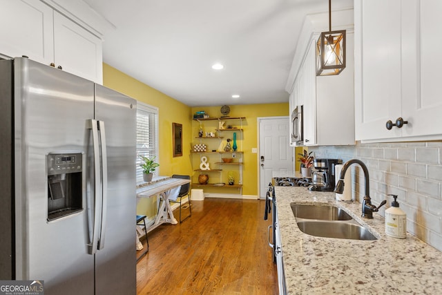 kitchen with pendant lighting, sink, backsplash, stainless steel appliances, and light stone counters