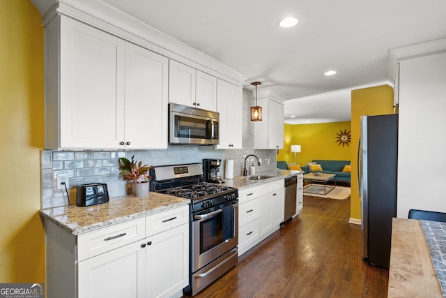 kitchen with appliances with stainless steel finishes, sink, white cabinets, hanging light fixtures, and dark wood-type flooring