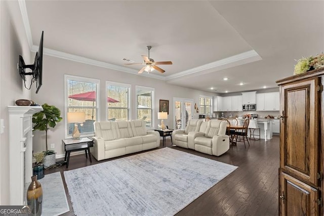 living room featuring crown molding, ceiling fan, a tray ceiling, and dark wood-type flooring