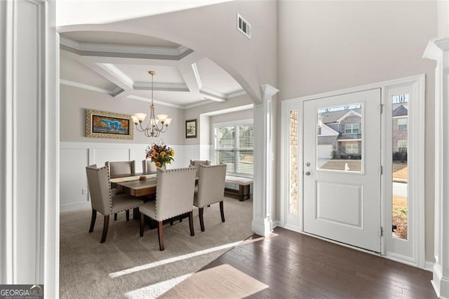 dining area featuring dark wood-type flooring, an inviting chandelier, coffered ceiling, ornamental molding, and beamed ceiling