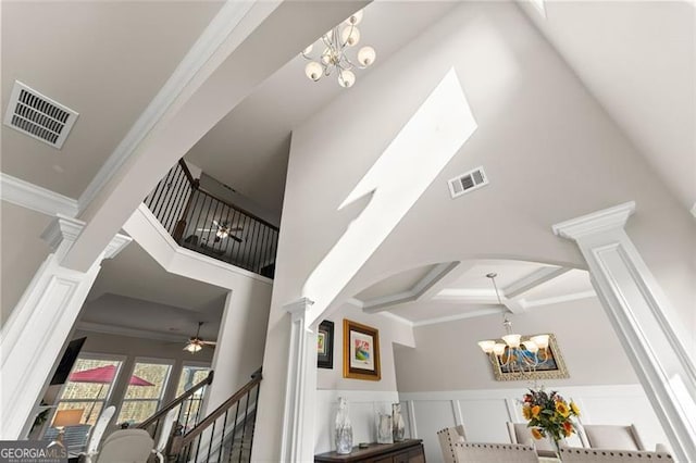 staircase with an inviting chandelier, crown molding, and decorative columns