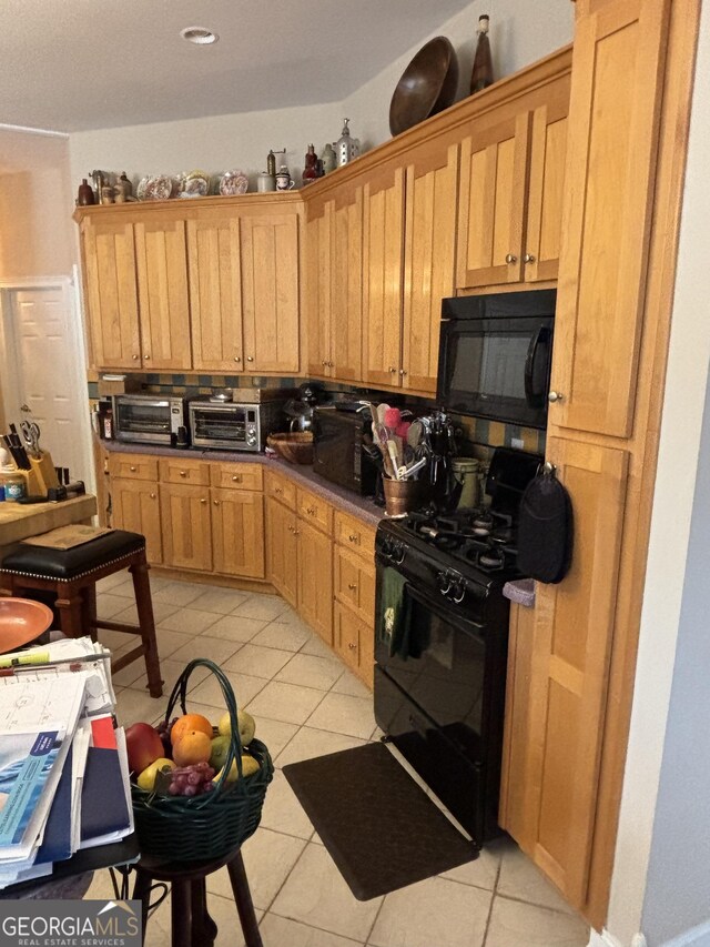 kitchen with black appliances, a toaster, light tile patterned flooring, and decorative backsplash