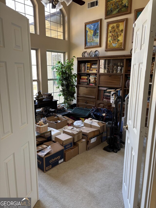 office area featuring carpet floors, visible vents, a towering ceiling, and a ceiling fan