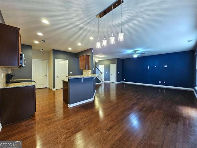 kitchen with pendant lighting, dark hardwood / wood-style floors, a kitchen breakfast bar, and light stone counters