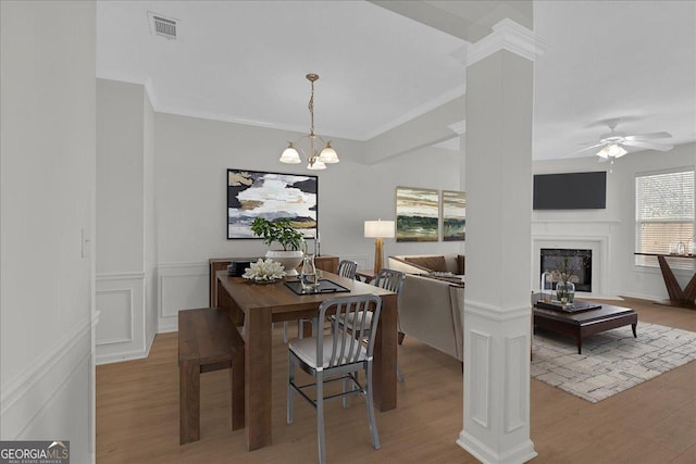 dining space with ceiling fan with notable chandelier, crown molding, light hardwood / wood-style floors, and ornate columns