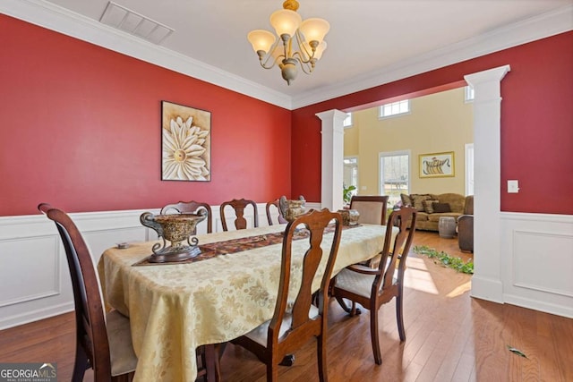 dining space featuring an inviting chandelier, hardwood / wood-style floors, crown molding, and ornate columns