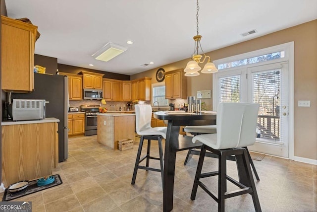 kitchen with pendant lighting, tasteful backsplash, appliances with stainless steel finishes, and a kitchen island