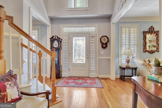 entryway with a towering ceiling, ornamental molding, and light hardwood / wood-style flooring