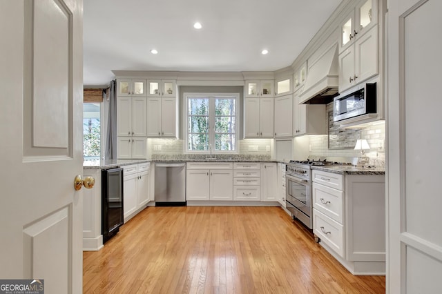 kitchen featuring wine cooler, custom exhaust hood, appliances with stainless steel finishes, light stone countertops, and white cabinets