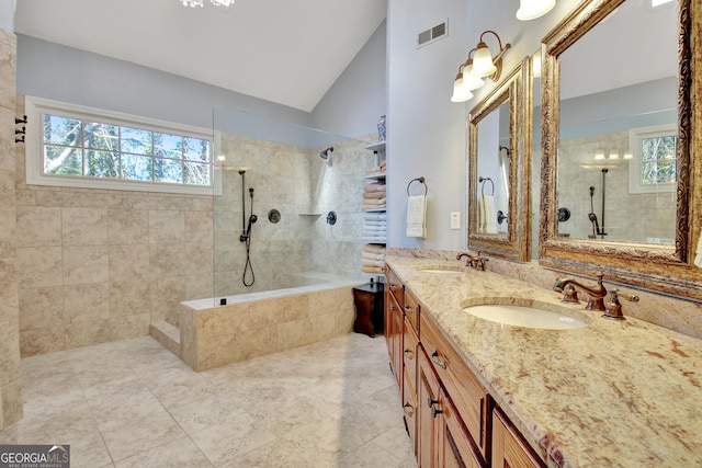 bathroom with vanity, a wealth of natural light, vaulted ceiling, and tiled shower