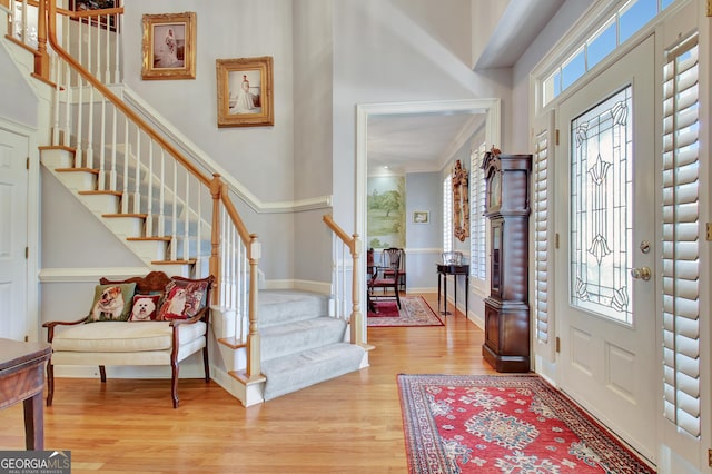 foyer entrance with a towering ceiling, ornamental molding, and light wood-type flooring