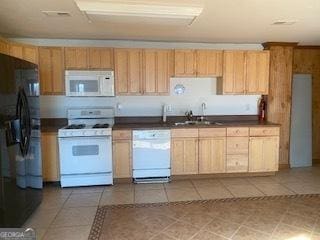 kitchen with dark countertops, white appliances, a sink, and light tile patterned flooring