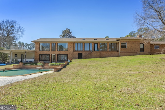 rear view of house with a yard, brick siding, and an outdoor pool