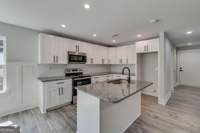 kitchen with electric stove, sink, stone counters, white cabinetry, and a center island with sink