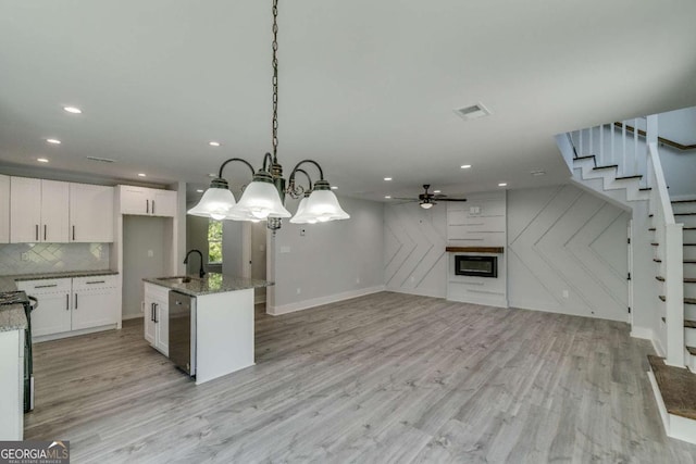 kitchen featuring pendant lighting, stainless steel dishwasher, a center island with sink, and white cabinets