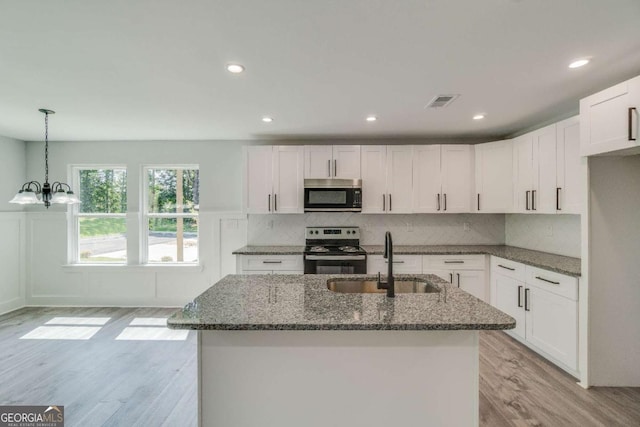 kitchen with sink, white cabinetry, hanging light fixtures, dark stone counters, and stainless steel appliances