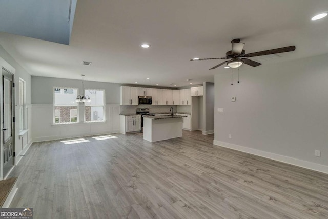 unfurnished living room with ceiling fan with notable chandelier, sink, and light hardwood / wood-style flooring