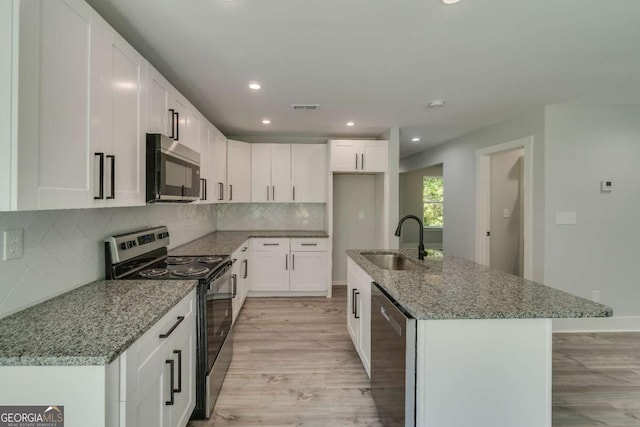 kitchen with sink, a center island with sink, appliances with stainless steel finishes, stone counters, and white cabinets