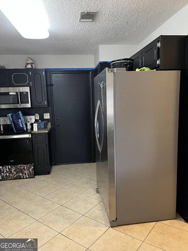 kitchen featuring stainless steel appliances, light tile patterned flooring, and a textured ceiling