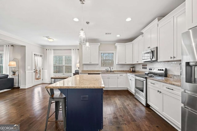 kitchen with light stone counters, white cabinetry, stainless steel appliances, and a center island