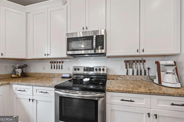 kitchen with light stone countertops, appliances with stainless steel finishes, white cabinets, and backsplash