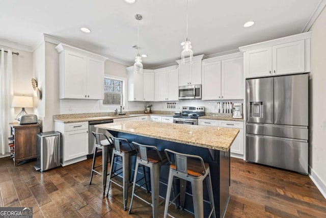 kitchen with appliances with stainless steel finishes, white cabinetry, hanging light fixtures, a center island, and light stone countertops