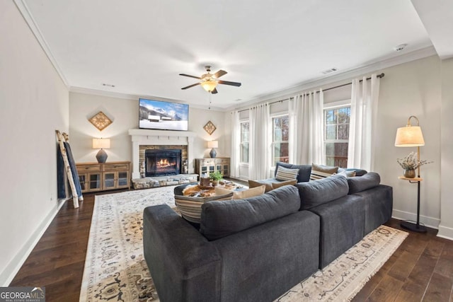 living room with crown molding, a stone fireplace, ceiling fan, and dark hardwood / wood-style flooring