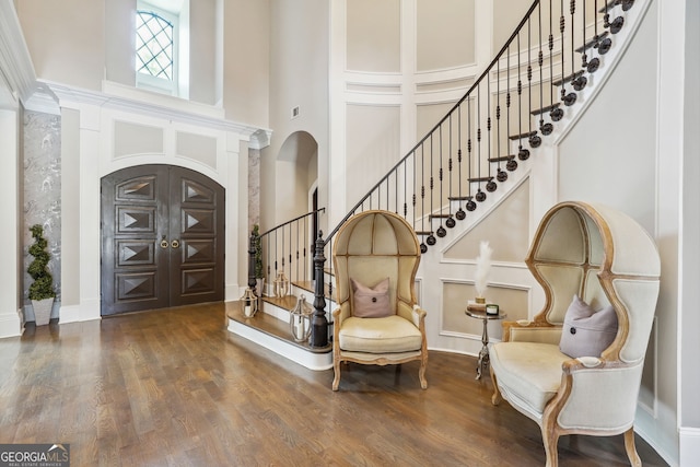 foyer entrance with a towering ceiling, stairway, arched walkways, and dark wood-type flooring