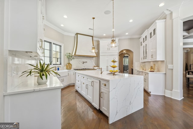 kitchen with an island with sink, arched walkways, white cabinets, and glass insert cabinets