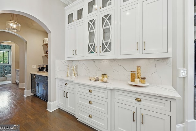 bar featuring arched walkways, dark wood-style flooring, backsplash, and baseboards