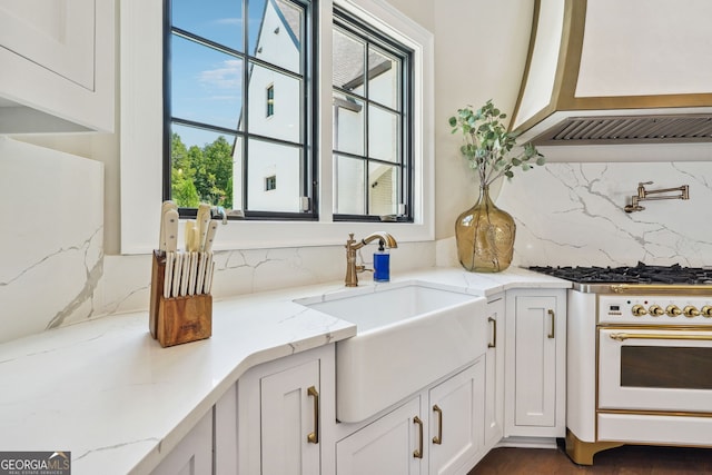 kitchen featuring tasteful backsplash, a sink, white cabinets, and light stone countertops