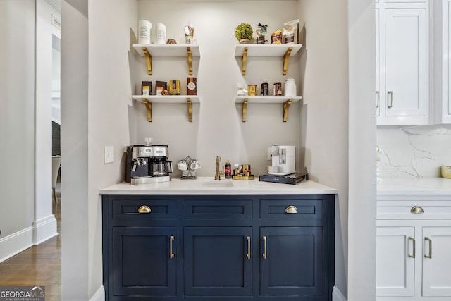 bar featuring dark wood-style floors, tasteful backsplash, baseboards, and a sink