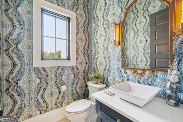 half bathroom featuring toilet, wallpapered walls, and vanity