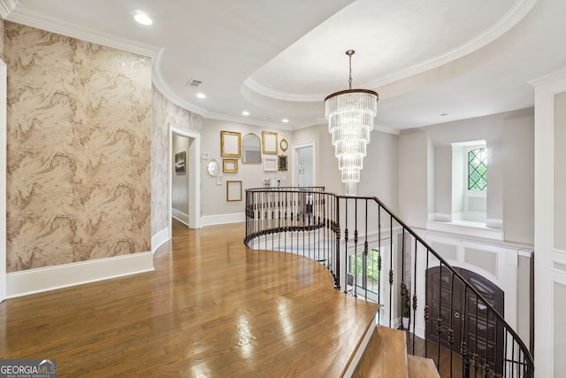 corridor with a raised ceiling, ornamental molding, an upstairs landing, wood finished floors, and a chandelier