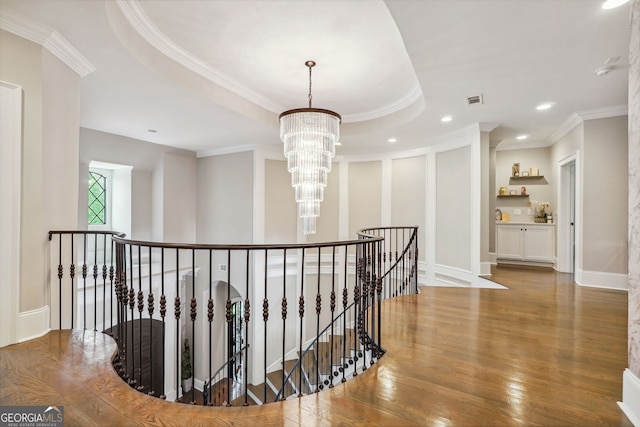 hall with a chandelier, wood finished floors, visible vents, an upstairs landing, and a raised ceiling