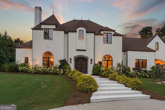 french provincial home with french doors, brick siding, a yard, and a chimney