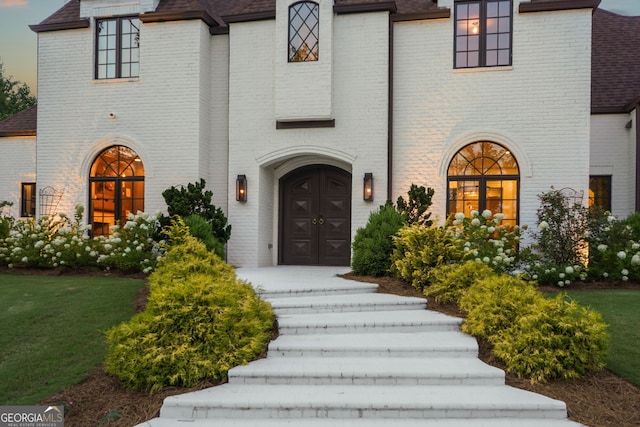 property entrance featuring roof with shingles and brick siding